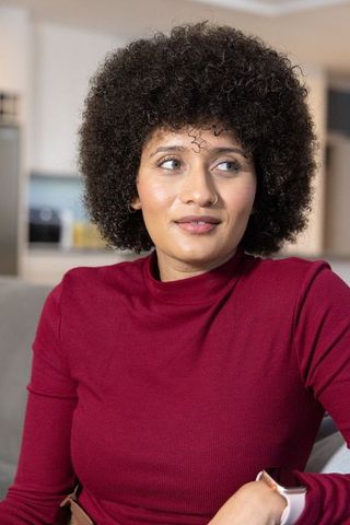 Young woman relaxing on sofa in burgundy top wearing smartwatch and nose ring casual home portrait
