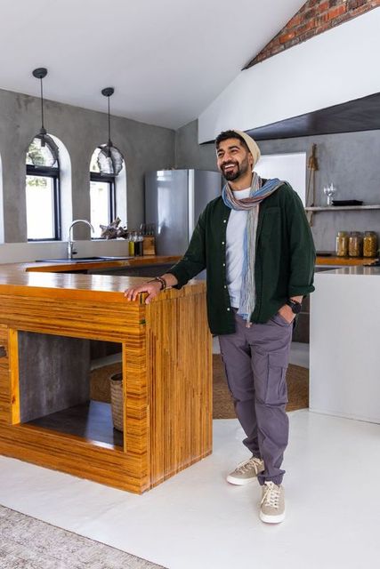 Man leaning on wooden kitchen island smiling wearing beanie and scarf in modern loft