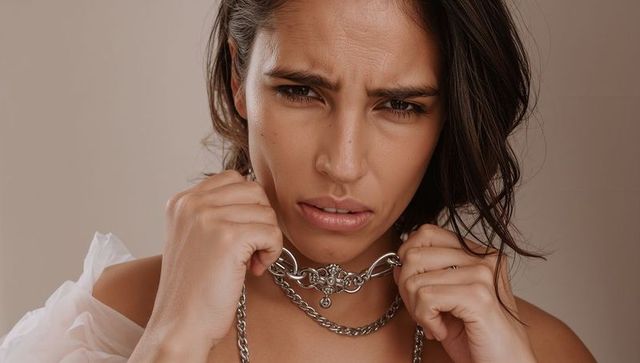 Tense woman gripping ornate chain necklace closeup, sheer off-shoulder garment