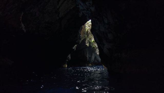 Triangular sea cave opening framing sunlit mossy rocks and sparkling water inside grotto