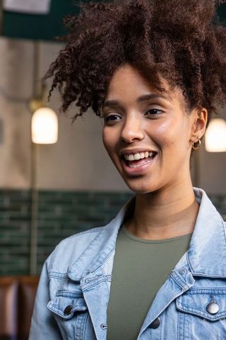 African american woman smiling and speaking in cafe wearing denim jacket