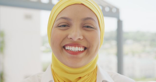 This vibrant close-up portrait of a smiling woman wearing a yellow hijab radiates happiness and positivity. It is perfect for use in advertisements focusing on joy, cultural diversity, and modern lifestyles. Websites and social media campaigns promoting fashion, personal well-being, and inclusivity can benefit from this image.
