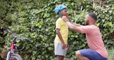 Father Ensuring Safety by Helping Son Wear Helmet, Happy Outdoor Moment