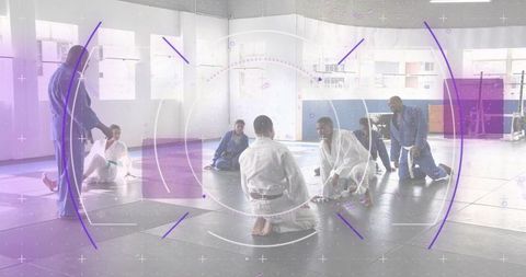 Teaching gi martial arts class with instructor guiding kneeling students on mats