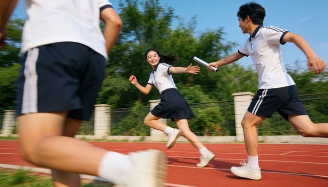 High school relay team passing baton on red track during sunny sprint