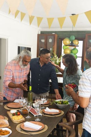 Seniors celebrating around dining table with charcuterie and wine, balloons