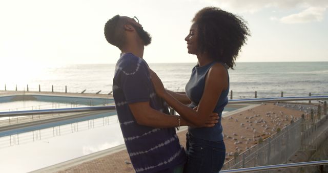 This stock photo captures a happy couple enjoying a moment together on a seaside balcony. They are sharing an intimate and cheerful moment, with the ocean and a clear sky in the background. Ideal for use in articles or advertisements focusing on romance, travel, or leisure. It evokes feelings of love and happiness and can be used to represent couples or relaxing outdoor activities.