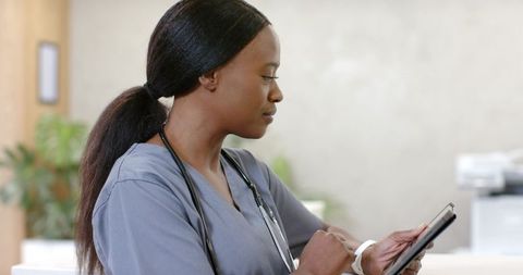 African nurse using tablet at clinic reception, reviewing digital records with stethoscope