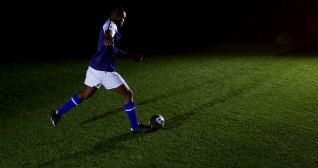 Soccer player dynamically kicking ball during nighttime match under bright stadium lights. Could illustrate sports action, athlete performance, and passion for football. Ideal for sports event promotions, athletic advertisements, and editorial content related to soccer games.