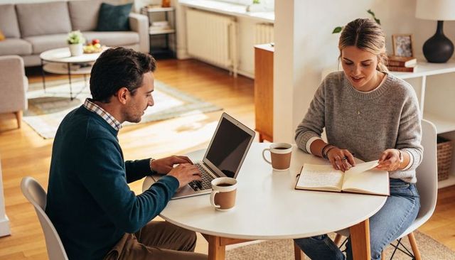 Couple working together at home office table using laptop and notebook, casual remote work