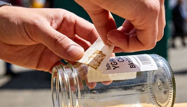 Peeling label from glass jar close-up hands removing sticker and adhesive residue sunlit