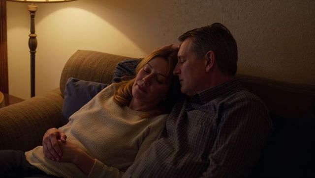 Middle-aged couple resting on couch at night under warm lamp light intimate cozy moment