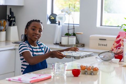 Preteen african girl baking cupcakes holding muffin tray in bright home kitchen
