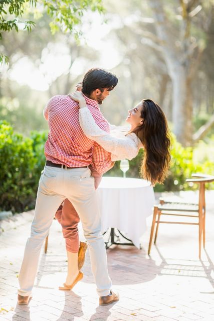 Couple dancing joyfully in a sunlit park, surrounded by greenery. Perfect for use in advertisements, romantic greeting cards, lifestyle blogs, and social media posts celebrating love and happiness.
