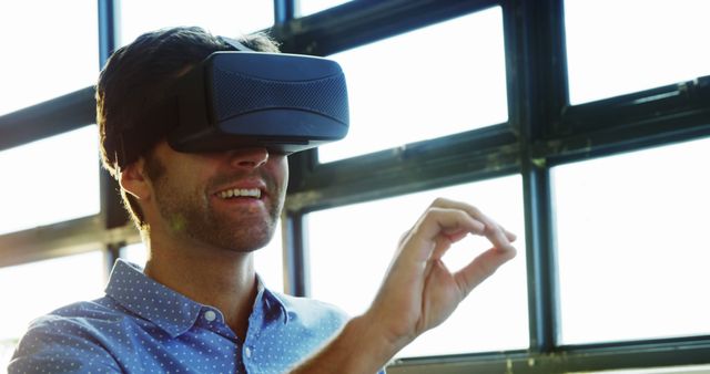 Man wearing VR headset, interacting with virtual environment in bright, modern room. Perfect for technology, gaming, innovation, and digital lifestyle themes.