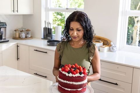 Indian woman presenting red velvet cake topped with fresh berries in bright kitchen