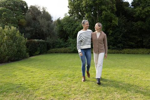 Mature women walking together on lush garden lawn sharing companionship and relaxed stroll