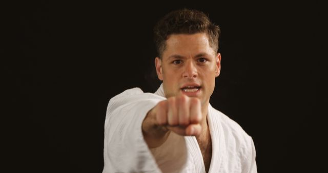 Martial artist punching while wearing a white gi, symbolizing focus and discipline in training. Suitable for use in articles or advertisements related to martial arts, self-defense classes, fitness programs, or motivational materials.