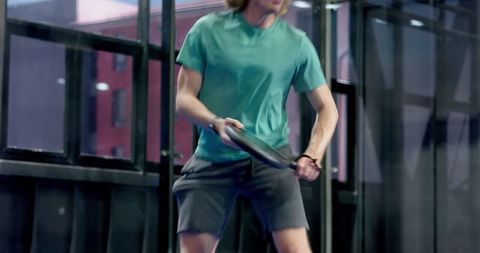 Athletic male playing paddle sport indoor glass wall facility