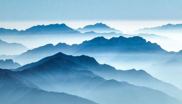 Receding mountain ridges fading into mist-filled alpine valleys under pale blue sky
