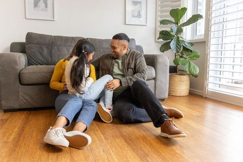 Parents and child laughing together on hardwood floor in sunlit living room