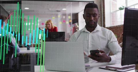 Checking smartphone while working on laptop in collaborative office with analytics overlay