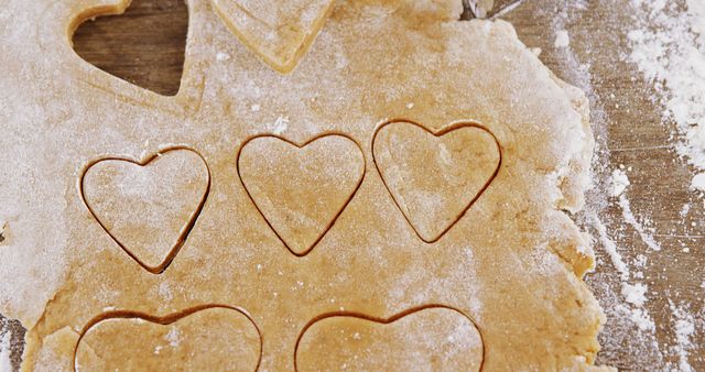 Heart-shaped cookie dough with flour on a wooden surface. Perfect for illustrating baking activities, Valentine's Day preparation, homemade pastries, and holiday-themed food articles.