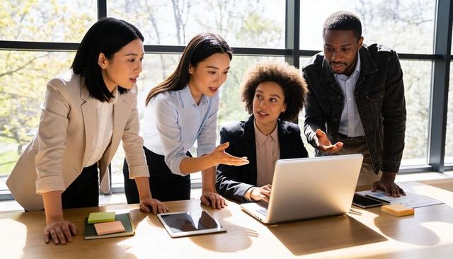 Multicultural team collaborating around laptop at wooden table in bright modern office