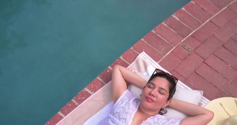 Sunbathing woman relaxing on towel by poolside with sunglasses and hat, overhead view