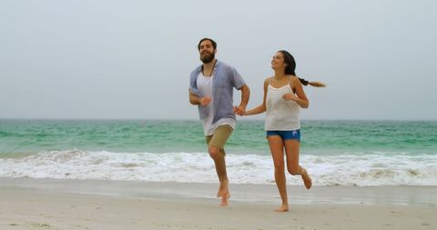 Happy Couple Running on Beach Holding Hands in Summer