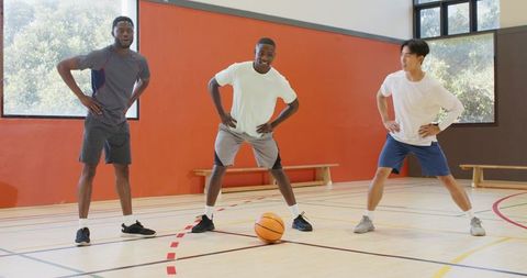 Diverse male teammates warming up on indoor basketball court performing lateral lunges