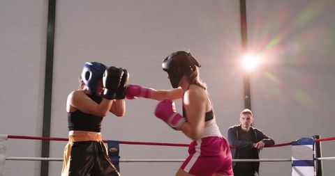 Female boxers sparring in ring with coach watching under dramatic backlight and flare