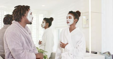 African american couple enjoying skincare routine in bright bathroom wearing robes