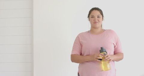 Smiling plus size woman holding water bottle indoors