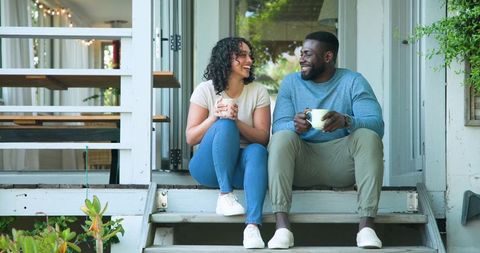Diverse couple enjoying coffee on cozy porch steps
