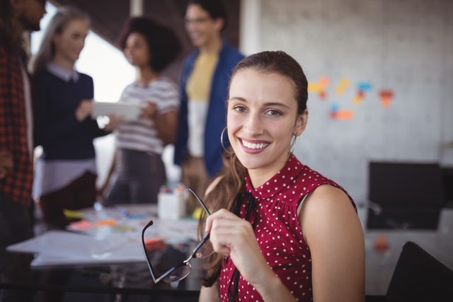 Smiling Businesswoman Holding Eyeglasses with Team in Background - Download Free Stock Images Pikwizard.com