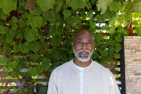 Senior african man standing in sunlit garden patio with lush vine trellis