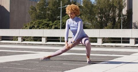 African American woman performing lateral lunge on rooftop in pastel leggings and smartwatch