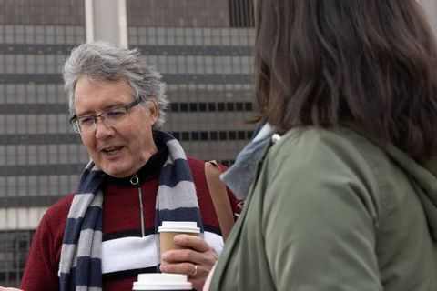 Senior man and female colleague chatting outdoors over takeaway coffee by office tower