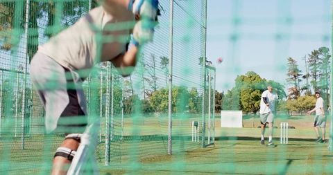 Teammates practicing batting in outdoor cricket nets on grass field team training session