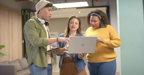 Diverse team collaborating around laptop in modern coworking lounge brainstorming ideas