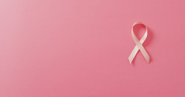 Image of pale pink breast cancer ribbon on pink background. medical awareness support campaign symbol for breast cancer.