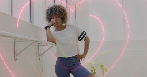Leaning woman on ballet barre showing smartwatch with neon heart overlay, fitness pose