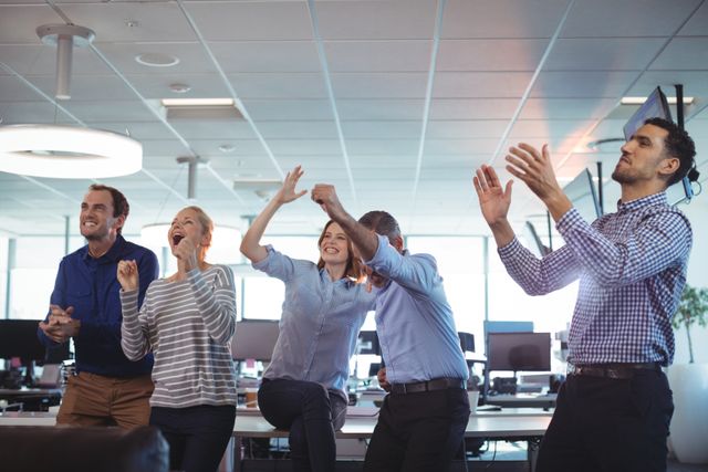 Group of business colleagues celebrating success in a modern office environment. Ideal for use in corporate presentations, team-building materials, motivational posters, and business success stories.