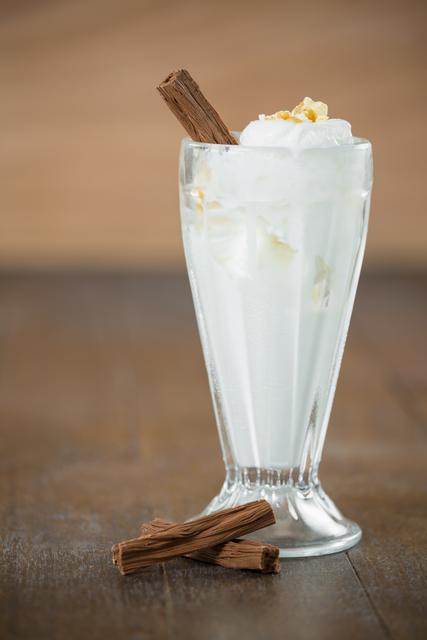 Vanilla ice cream served in a tall glass, garnished with a chocolate stick, placed on a wooden table. Ideal for use in food blogs, dessert menus, summer refreshment promotions, or gourmet recipe books.
