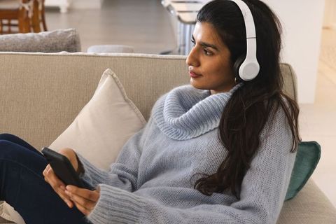 Asian Woman Using Headphones Relaxing on Sofa with Smartphone
