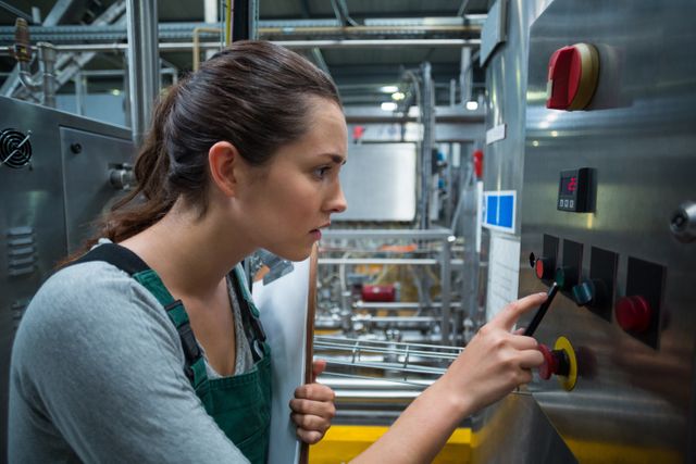Female factory worker operating heavy machinery in an industrial bottle factory. She carefully presses buttons on the control panel, ensuring machinery functions correctly. Useful for illustrating industrial work environments, manufacturing processes, factory automation, and workplace safety.