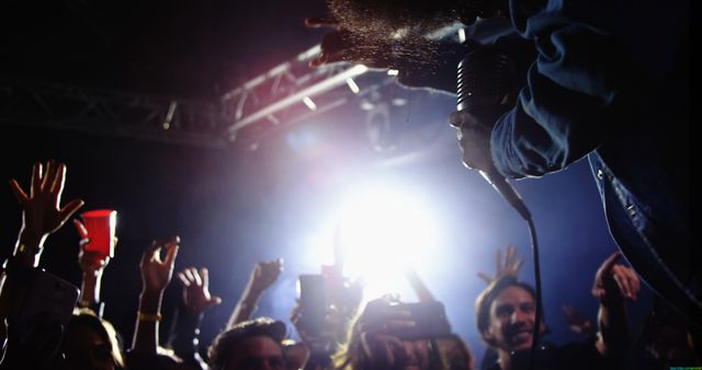 A performer engages with an enthusiastic crowd at a concert, with copy space. Bright stage lights illuminate the diverse audience as they reach out towards the artist.
