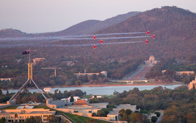 This vibrant capture features a thrilling aerial performance by fighter jets over Canberra's iconic landmarks at sunset. The Australian flag, Parliament House, and National War Memorial are clearly visible. Ideal for use in travel publications, educational materials, or patriotic Australian content.