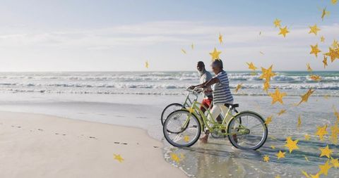 Senior couple walking bikes along sunlit beach with golden star overlay and footprints